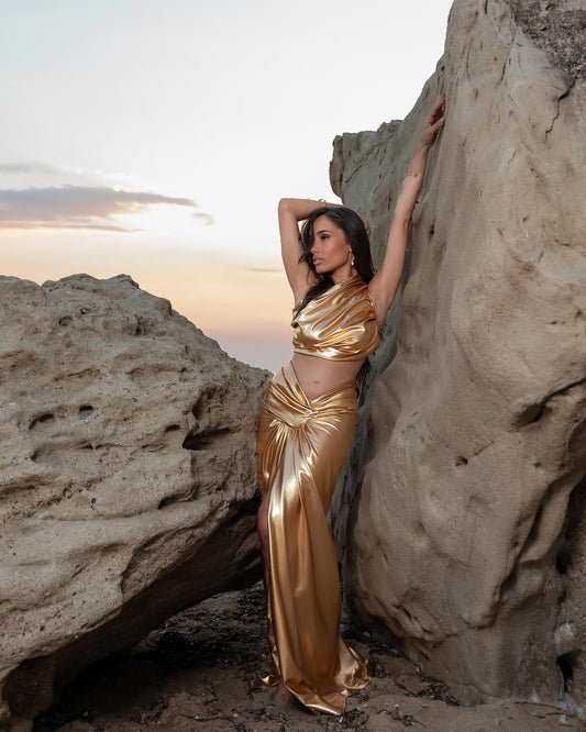 Woman posing between large rocks at sunset wearing a shiny gold dress with cutouts