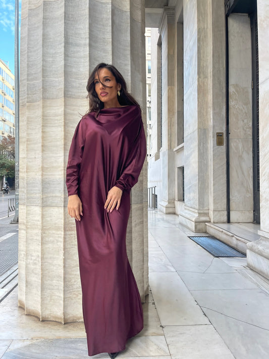Woman in elegant burgundy satin dress standing by tall marble columns outdoors