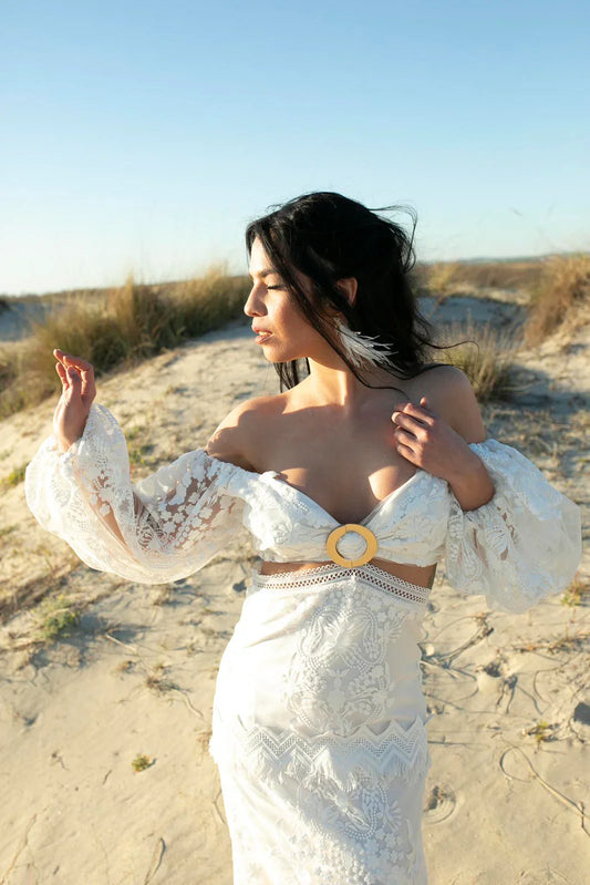 Woman in white lace off-shoulder dress with puff sleeves standing on sunny sandy beach
