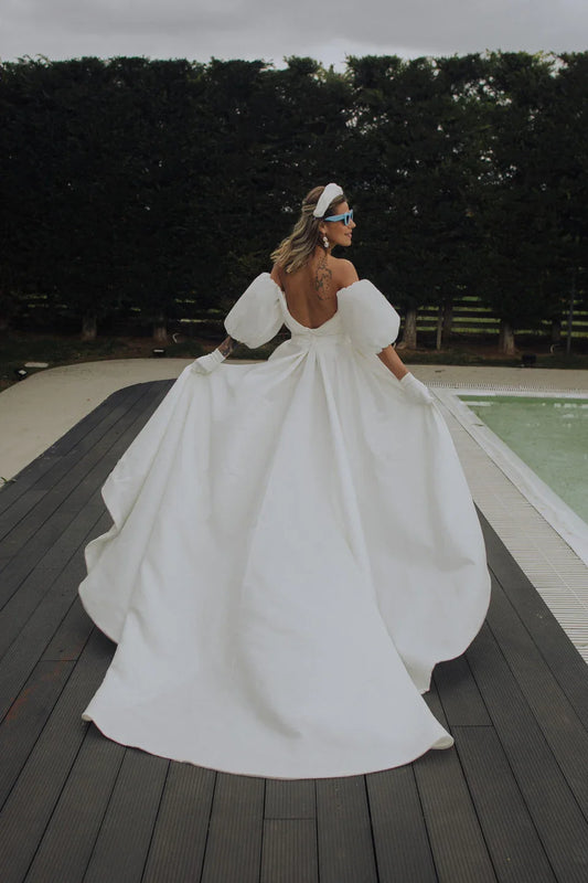 Woman in white off-shoulder gown with puffy sleeves and gloves by poolside wooden deck