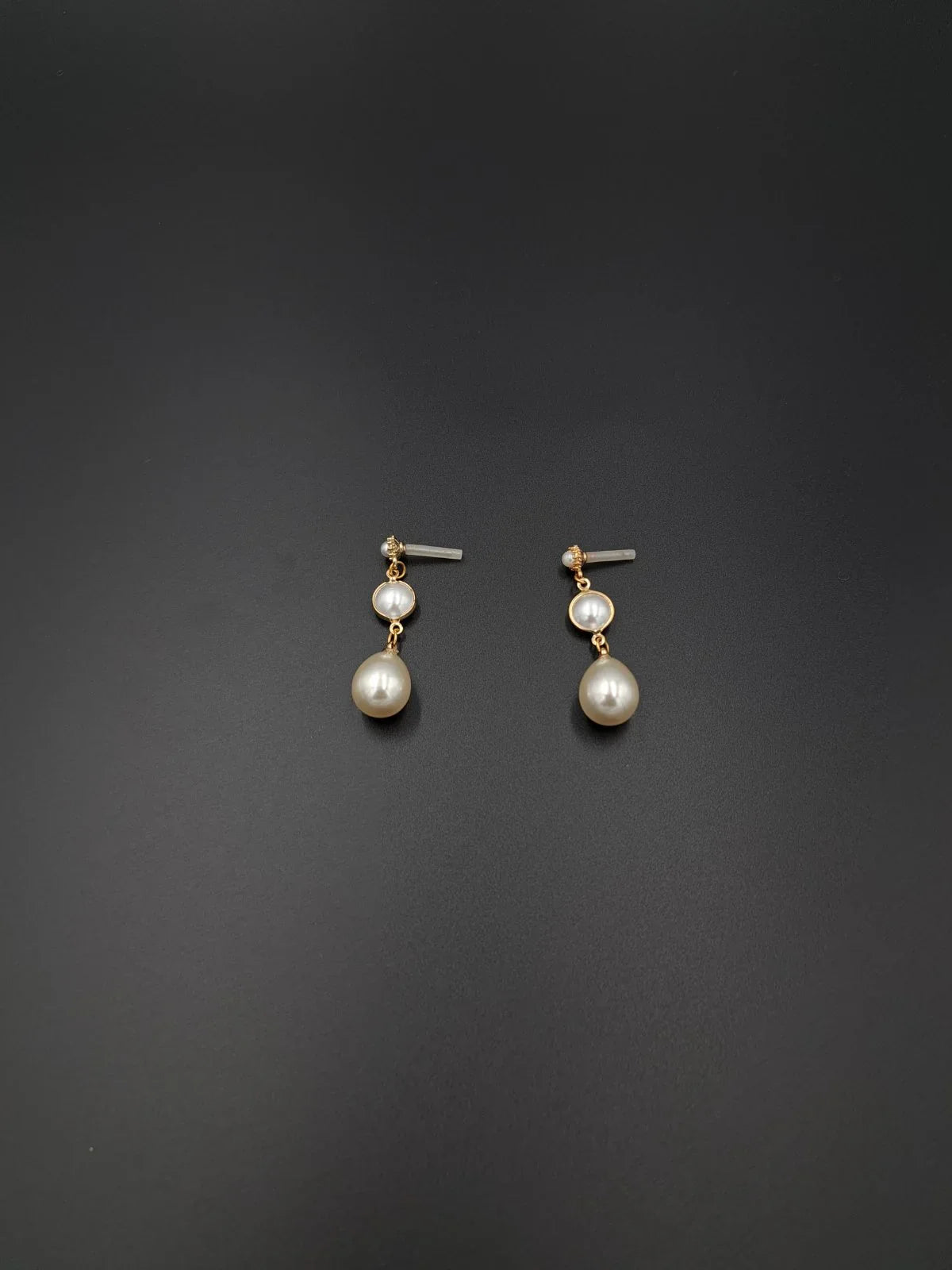 Pair of gold and pearl drop earrings with round and teardrop pearls on black background