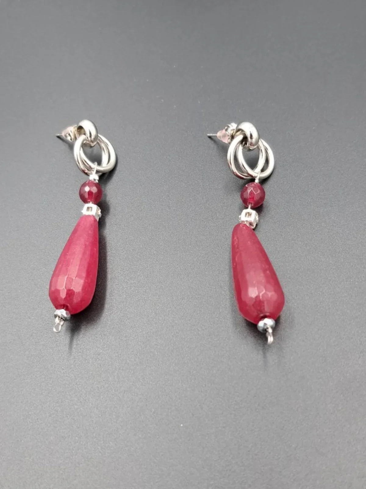 Silver loop earrings with red faceted teardrop and round beads on dark gray background