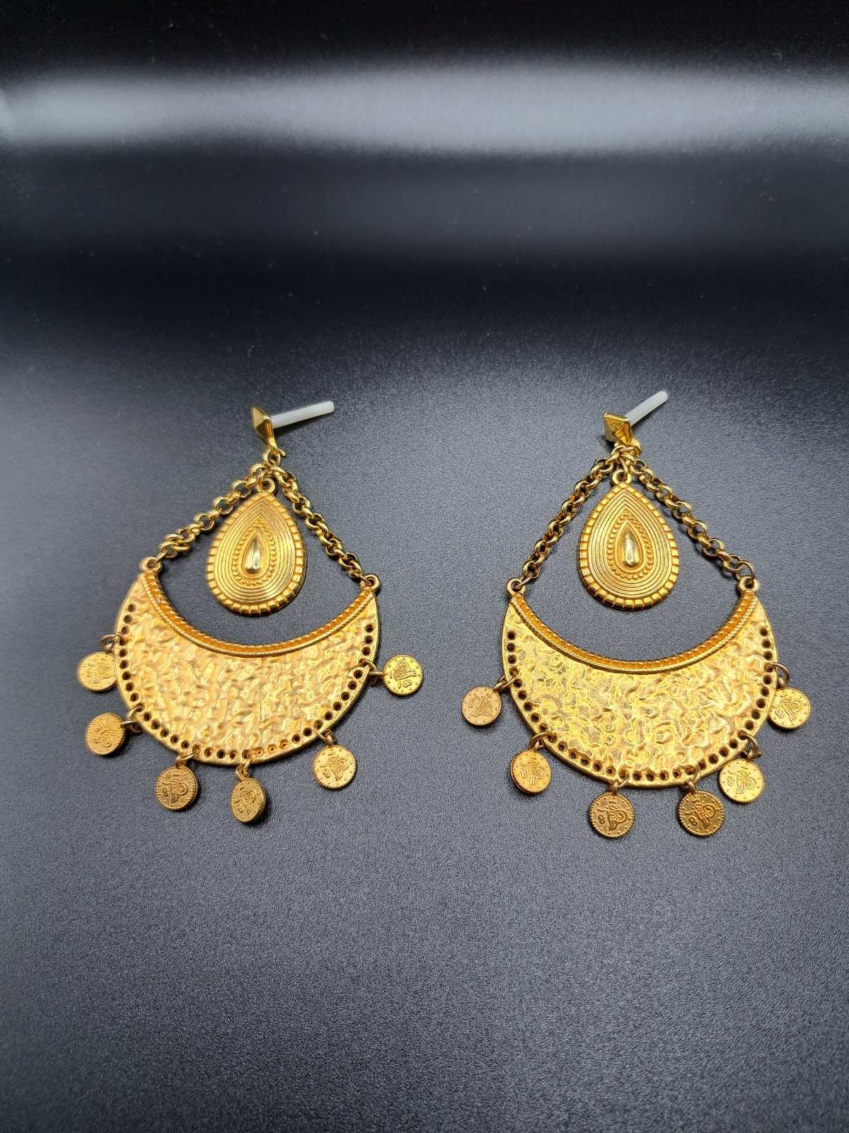 Pair of intricate gold-tone ethnic chandelier earrings with teardrop and coin charms on black background