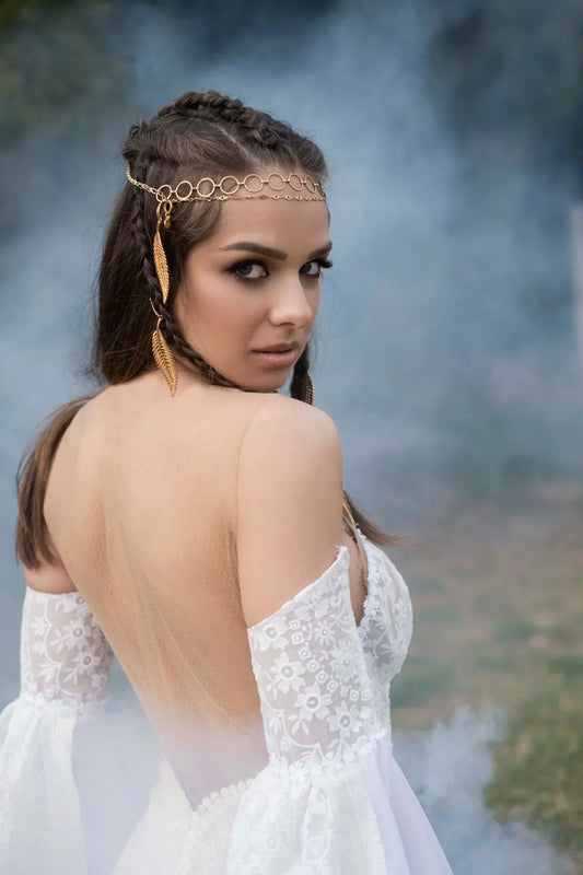 Woman in white lace off-shoulder dress with braided hair and gold chain headpiece in smoky outdoor setting