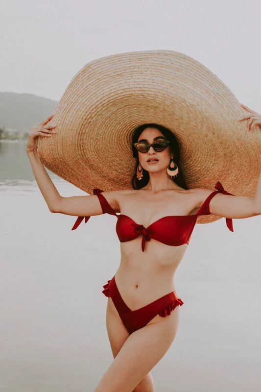 Woman in red bikini and oversized straw hat posing by serene lake with mountains in background