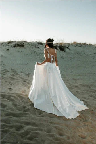 woman wearing a flowing white backless dress standing on sandy dunes under clear sky