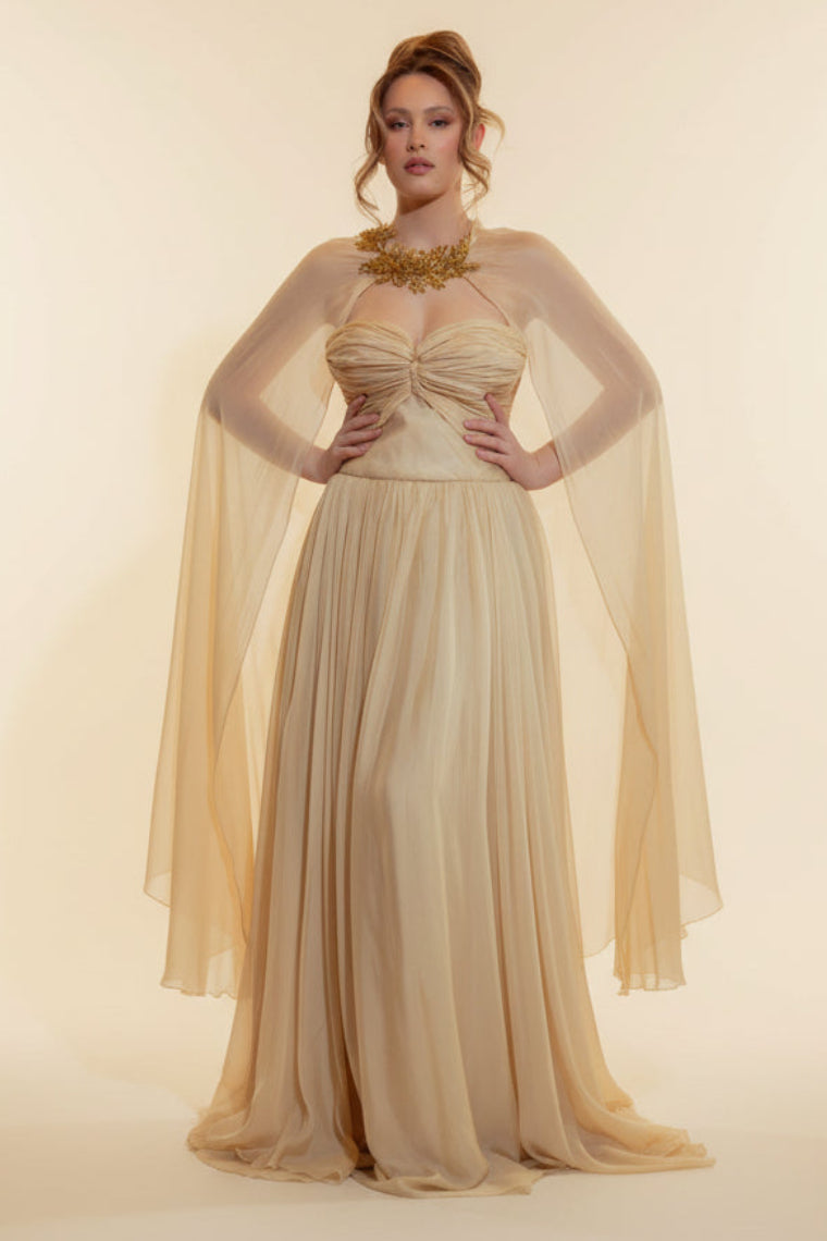Woman in a beige evening gown standing in a room with a large mirror and red walls.
