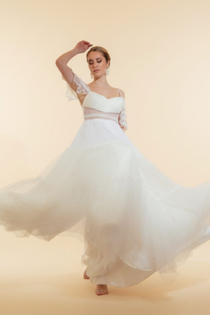 Woman in a white dress dancing in a room with a chandelier and floral arrangement.
