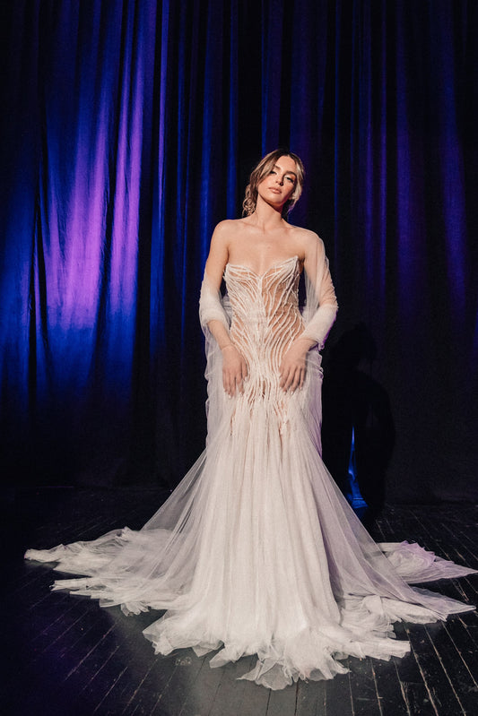 Woman in a white wedding dress standing against a dark curtain background