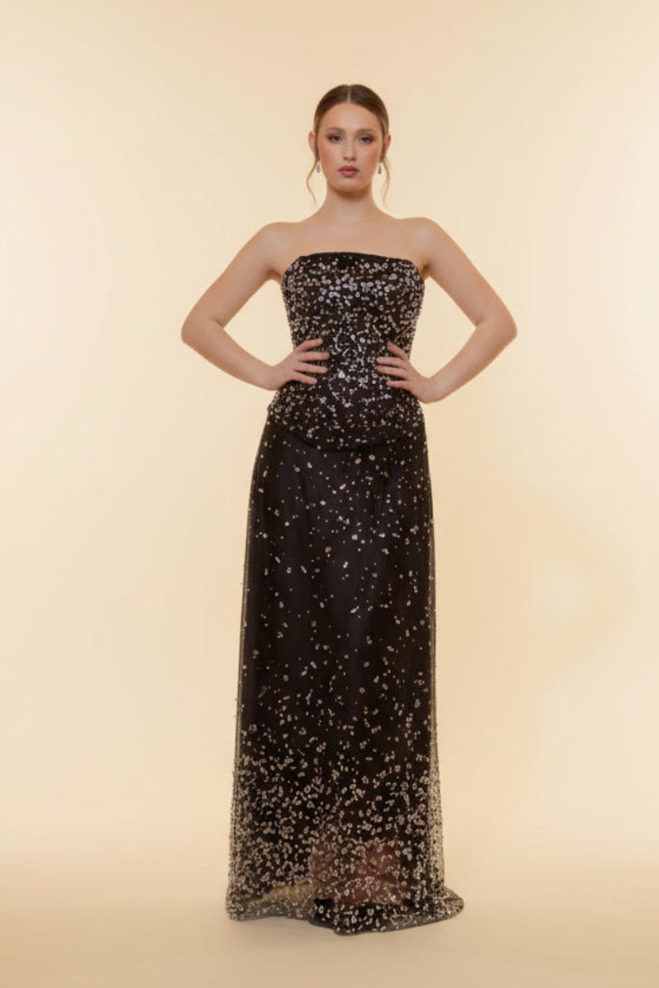 Woman wearing a black strapless evening gown with gold embellishments on a beige background