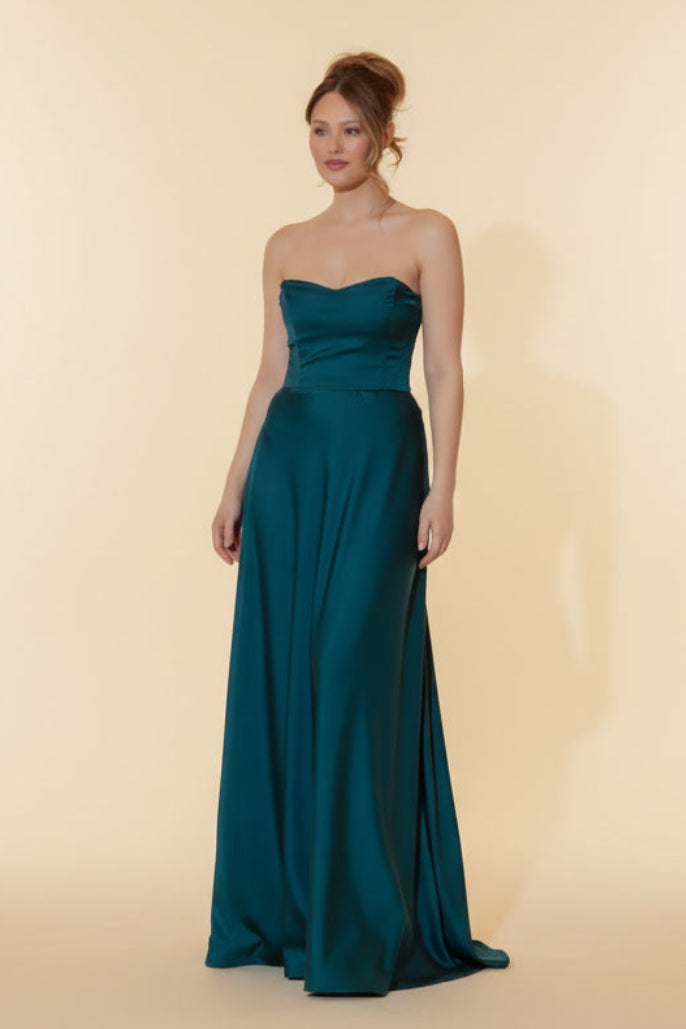Woman wearing a teal strapless gown against a beige background