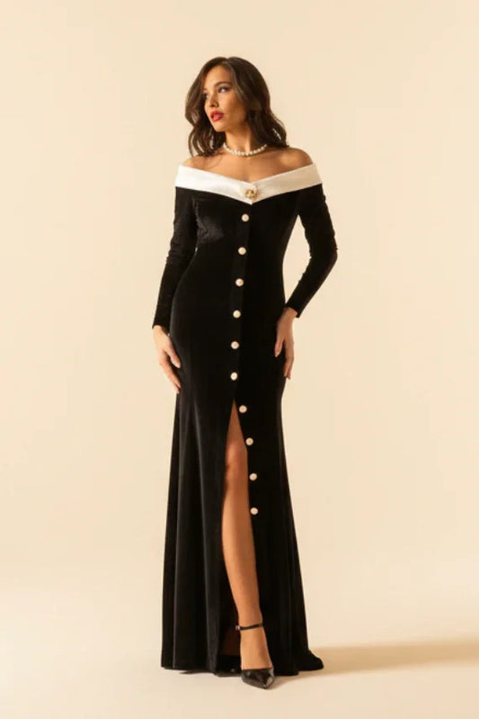 A woman standing in a columned hallway wearing an off-white princess collar black formal dress with golden and white pearl buttons.