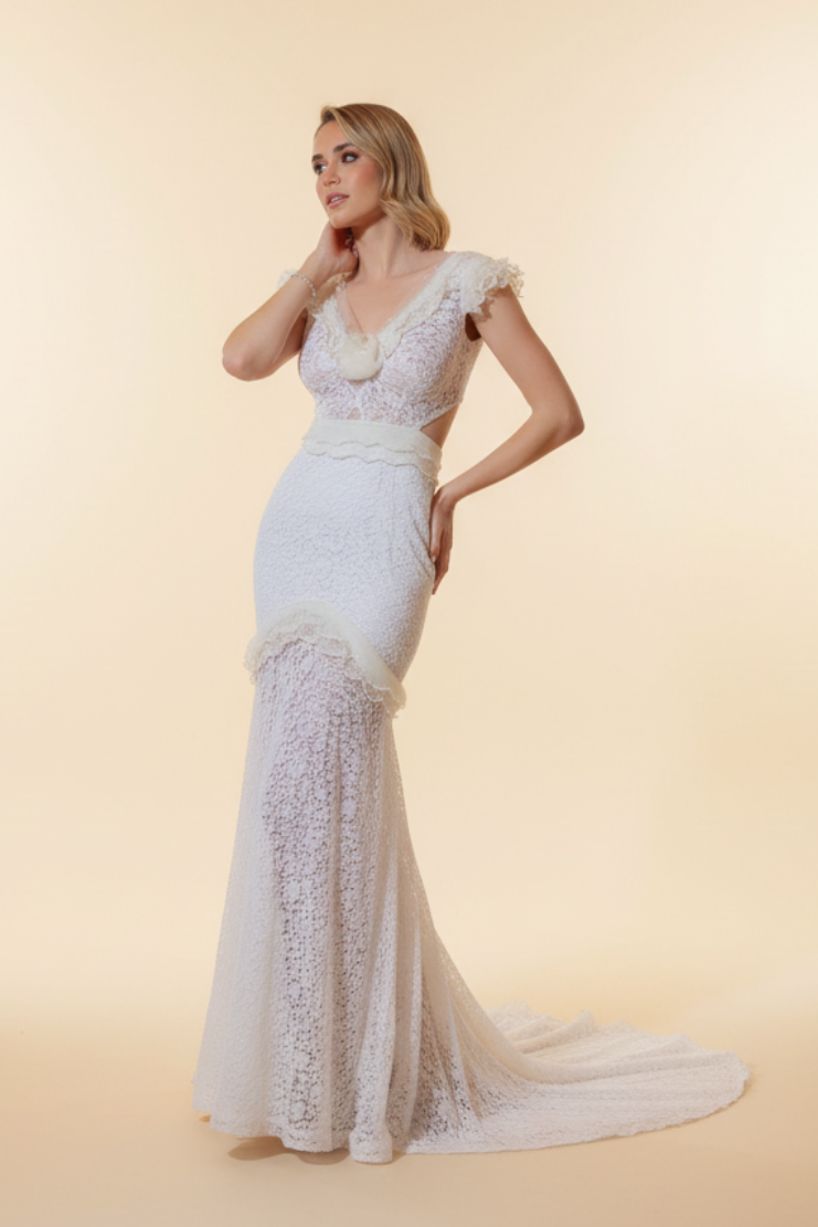 Woman in a white lace dress standing in front of an ornate mirror in a decorated room.