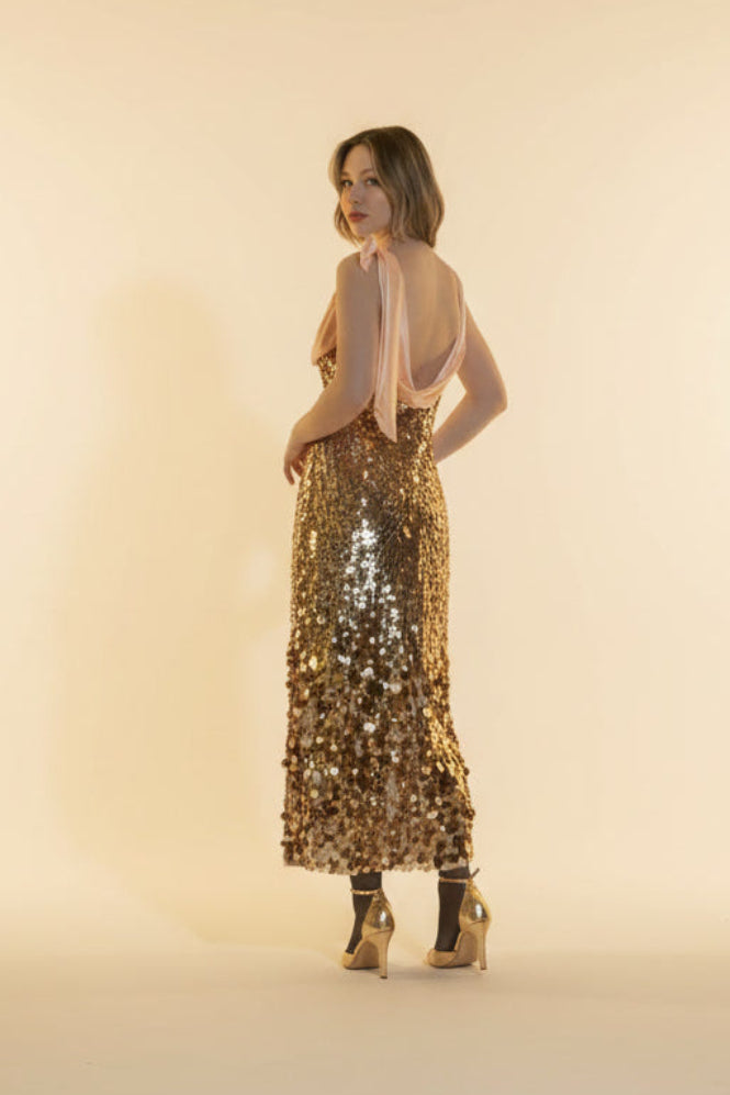 Woman wearing a gold sequin dress against a beige background