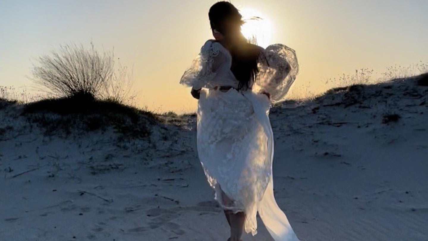 Person in a white dress running on a sandy beach with a sunset in the background